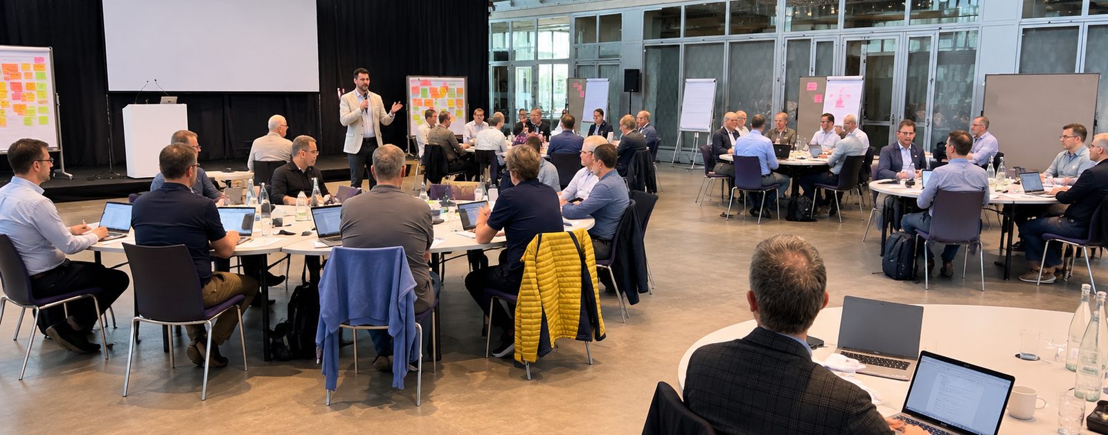 Steven Käser spricht vor einem grossen Leadership-Training, Leinwand und Tischgruppen im Saal